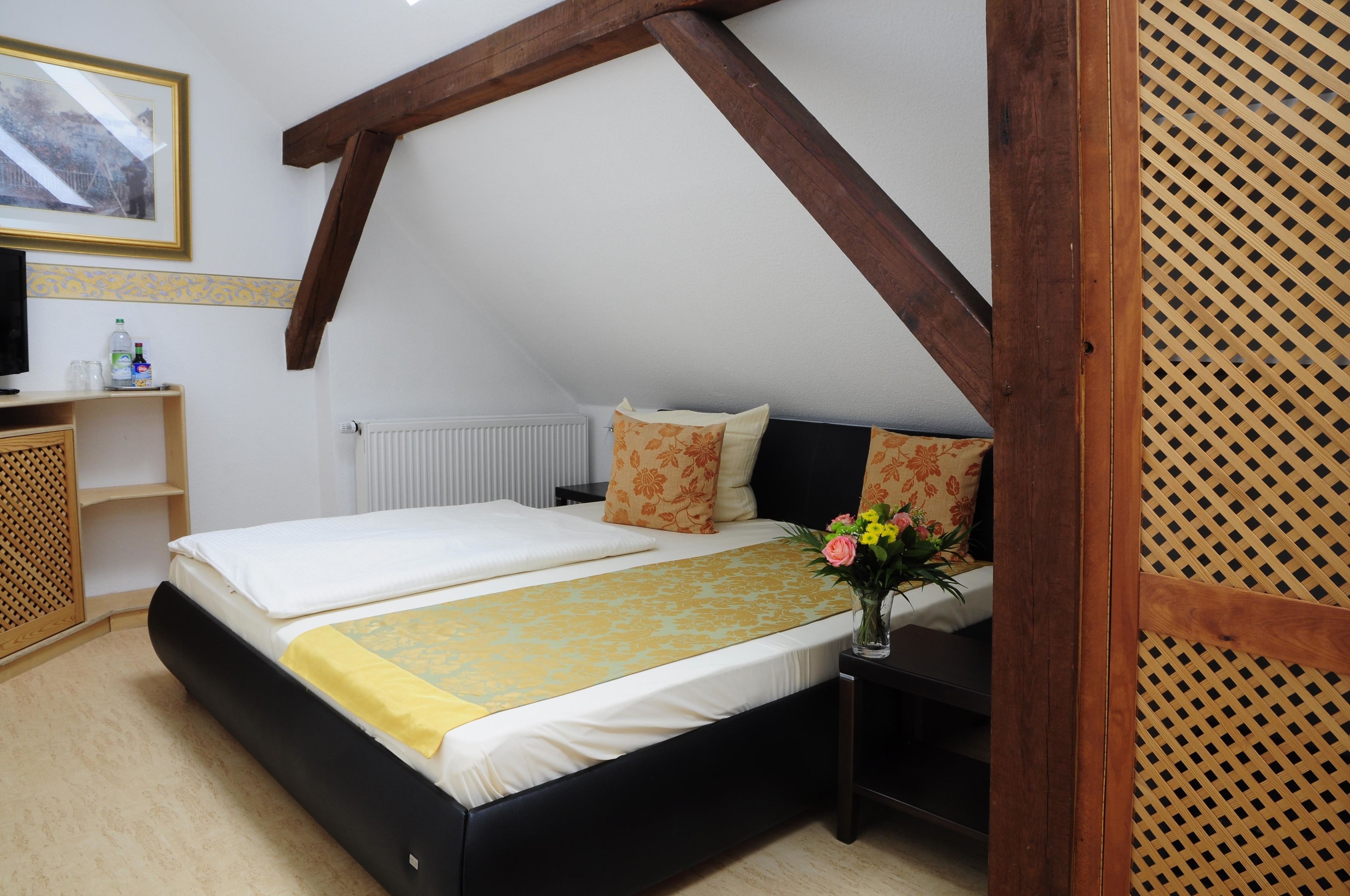 Un dormitorio con cama, mesita de noche, un florero y una viga de techo de madera.
