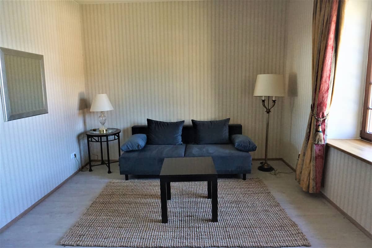 Ein Wohnzimmer mit einer Couch, zwei Beistelltischen, einem Couchtisch und einem Fenster mit Vorhängen.