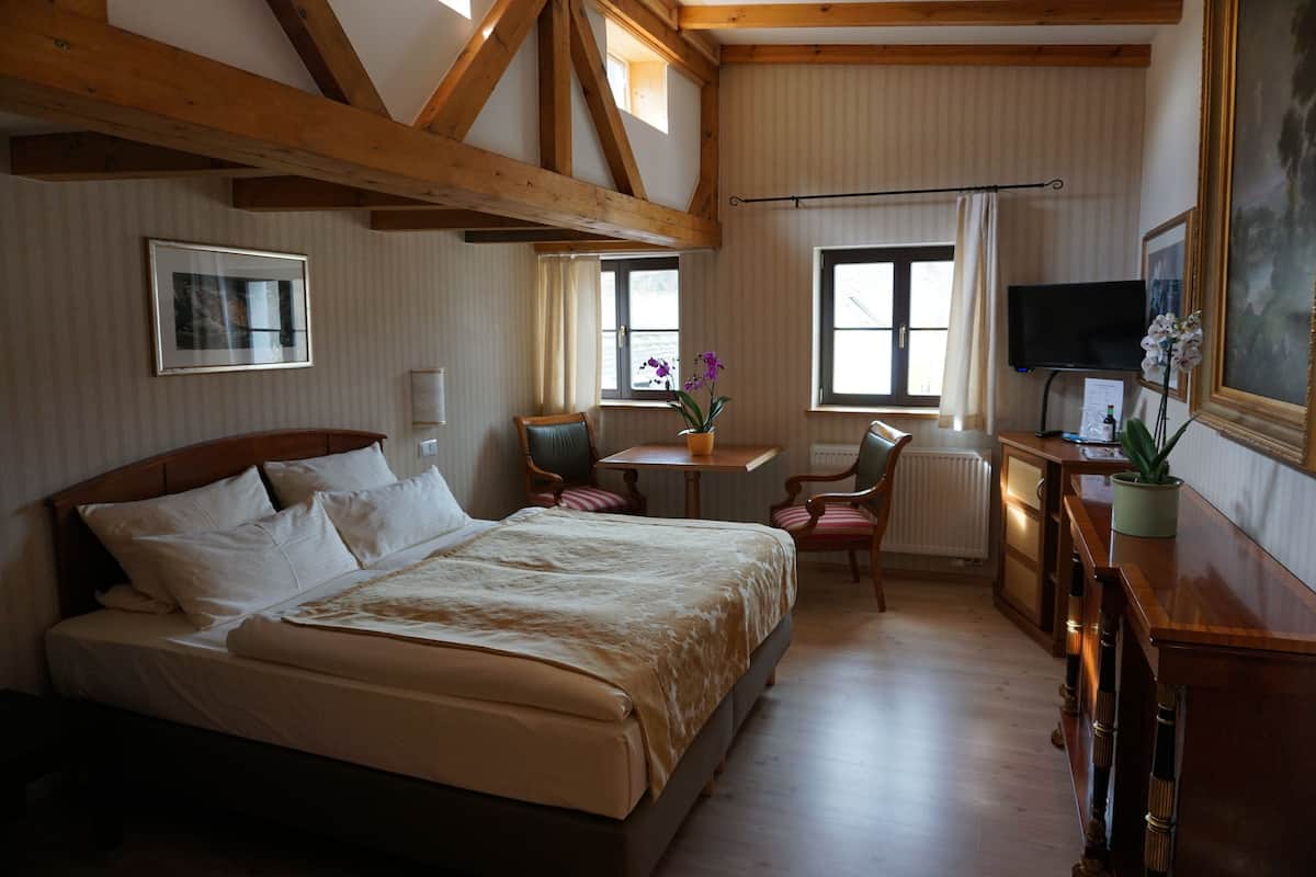 Ein Hotelzimmer mit einem großen Bett, einem Schreibtisch mit Stuhl, einem Fernseher und einem Fenster mit Vorhängen.