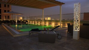 Un área de piscina en la azotea con sillones, bar y pérgola.