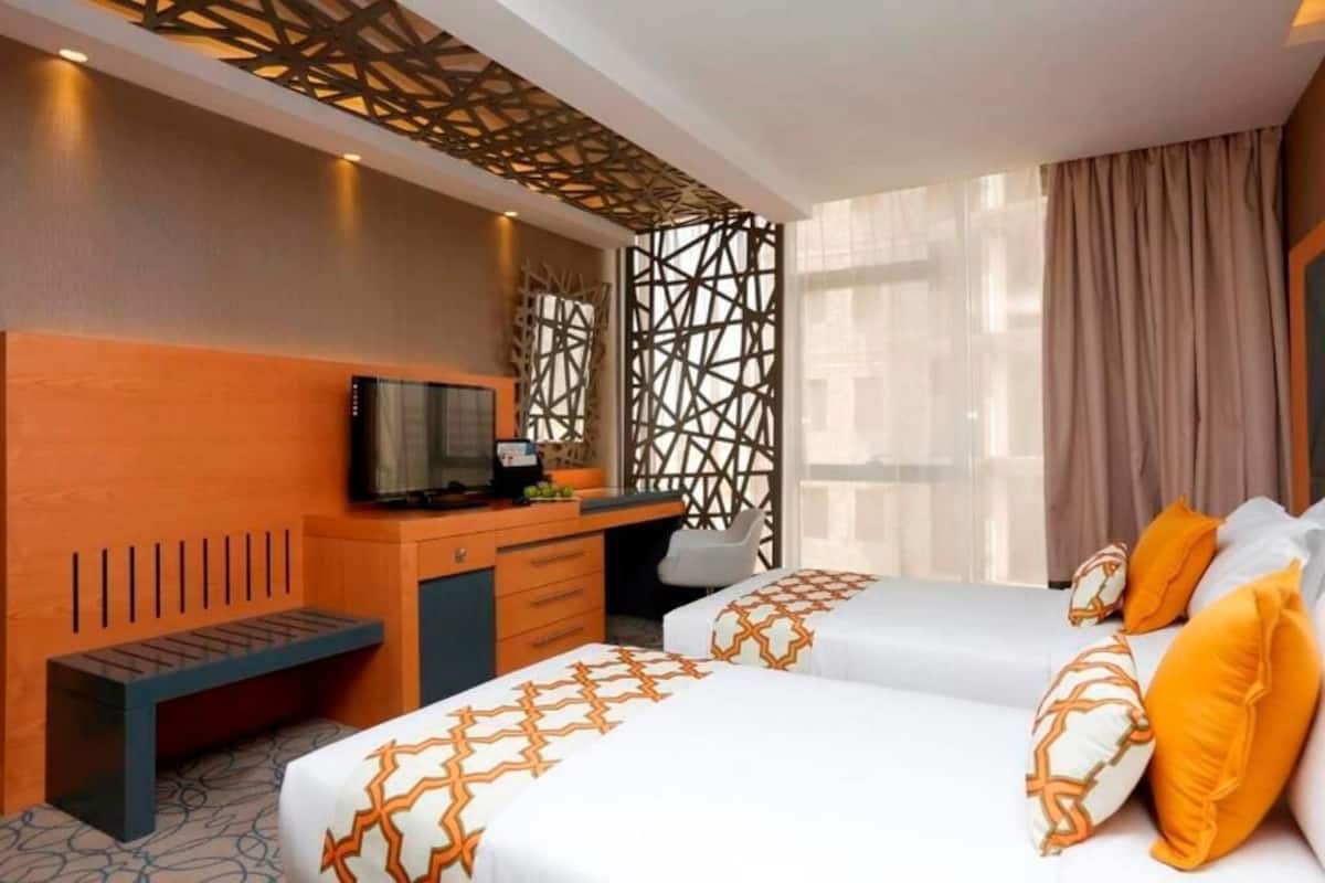 Ein Hotelzimmer mit zwei Betten, einem Schreibtisch mit Fernseher und einem dekorativen Raumteiler.