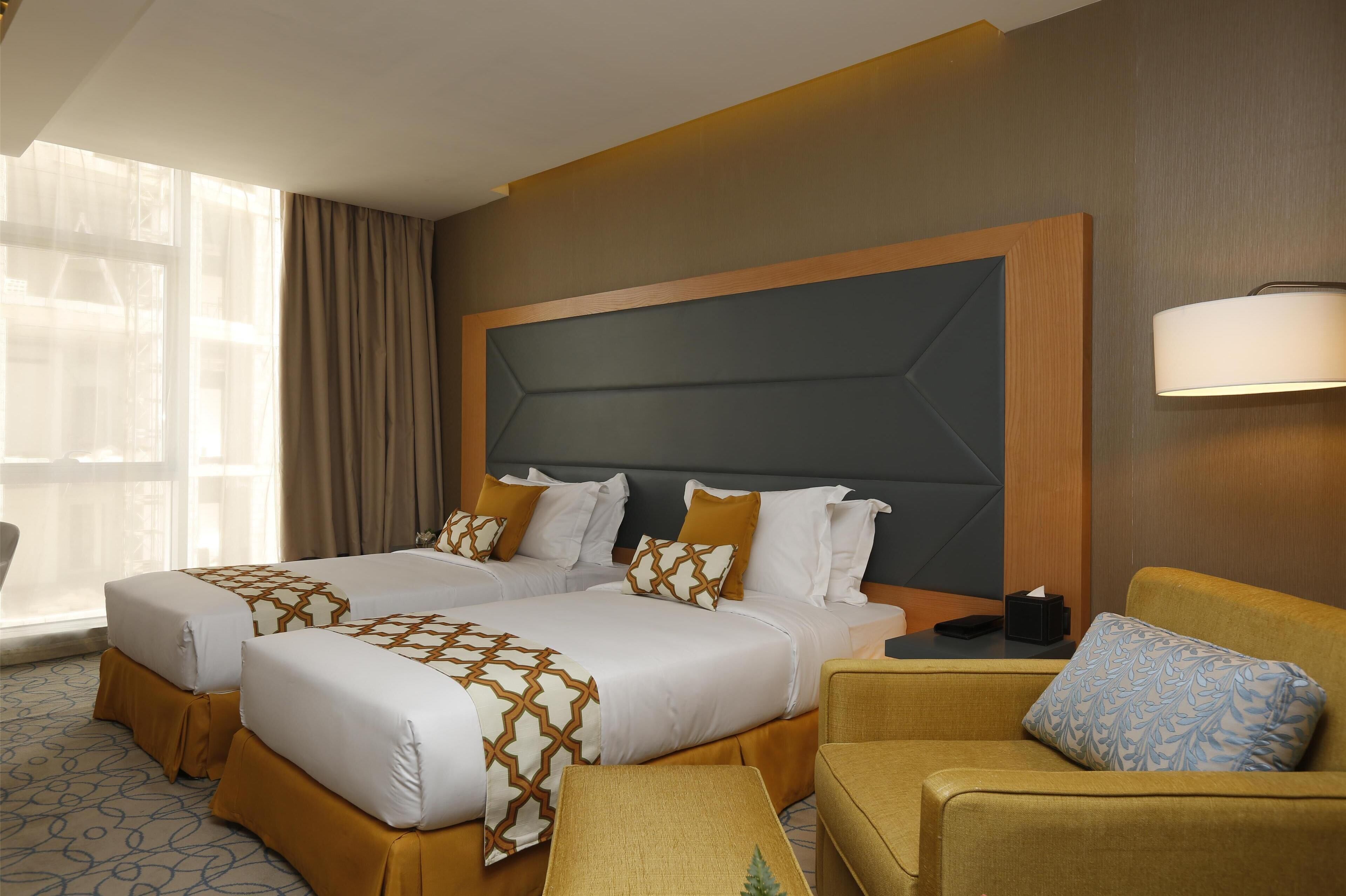 A hotel room with two beds, a sofa, and a bedside table.