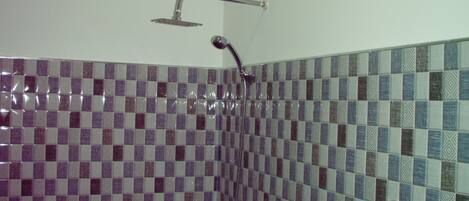 A shower with a handheld showerhead and a wall-mounted faucet. The shower area has tiled walls with a checkered pattern.