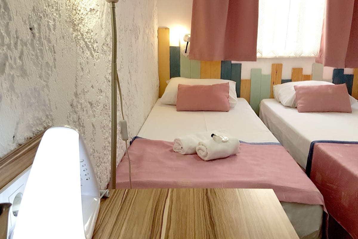 A hotel room with two beds, each with a pink bedspread and pillows. There is a wooden table in the center of the room.
