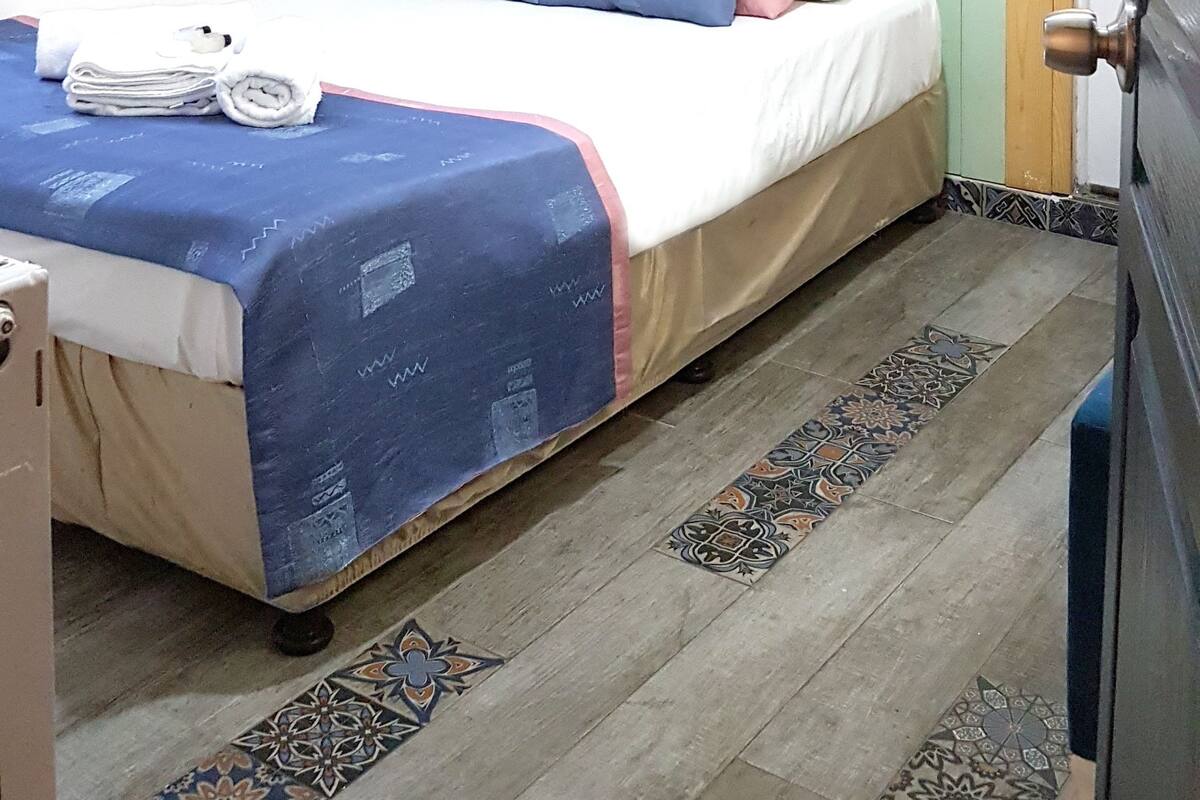 A bedroom with a bed, pillows, a painting, a curtain, and a patterned rug.