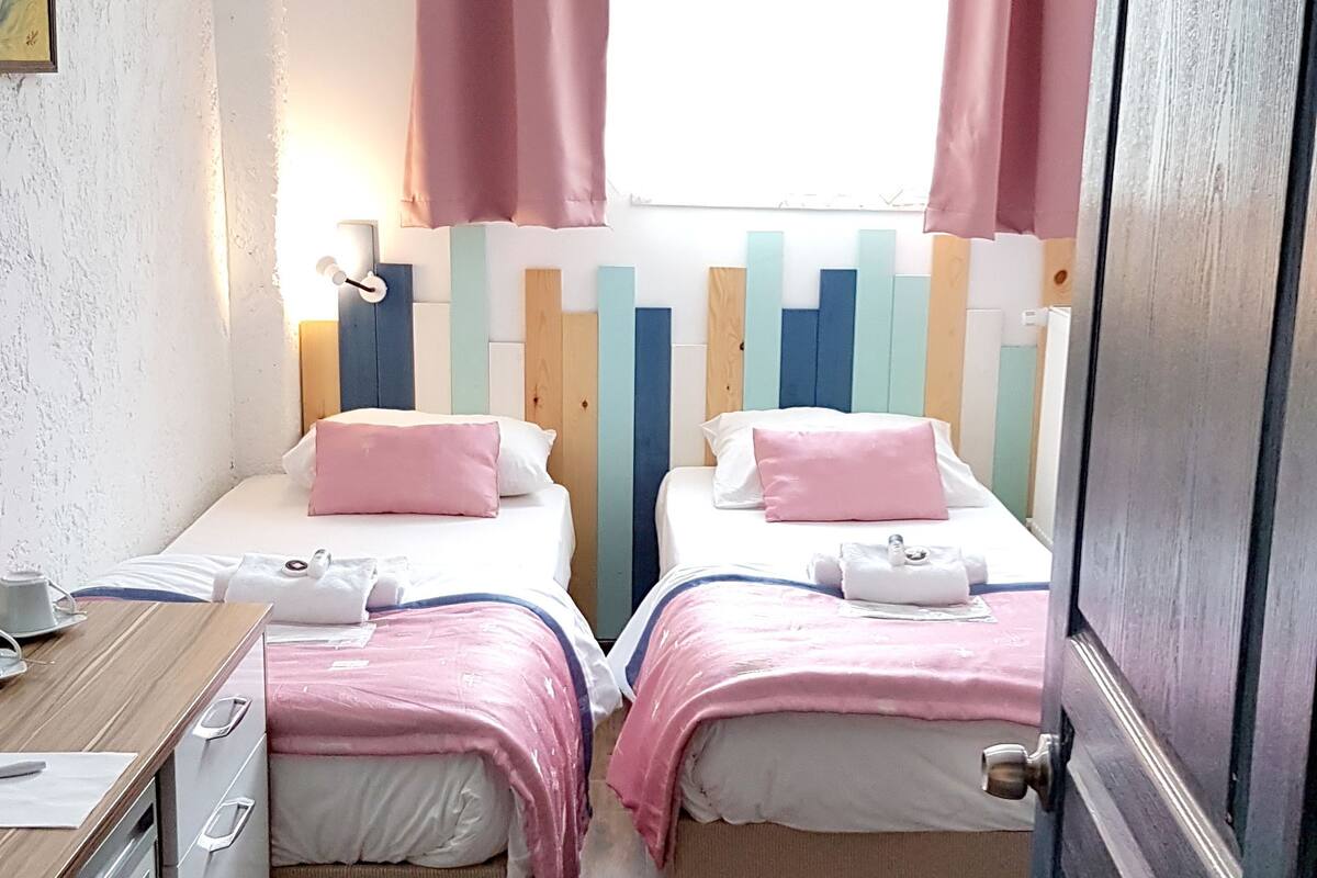 A room with two beds, a desk, a window with curtains, and a door.