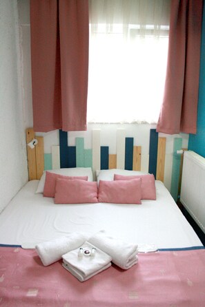 A neatly made bed with pink and white bedding, a wooden headboard, and a window with pink curtains. - AlaDeniz Hotel (Istanbul)