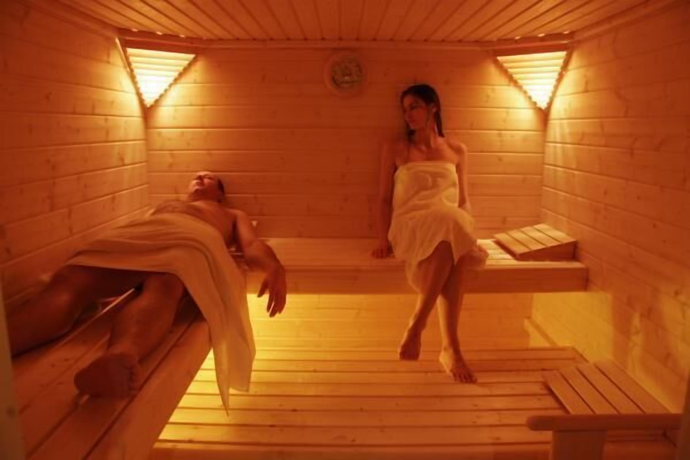 A sauna room with wooden benches and benches, a bench with a towel, and a bench with a person lying down.