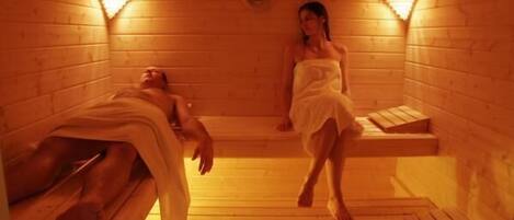A sauna room with wooden benches and benches, a bench with a towel, and a bench with a person lying down.