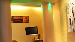 A cozy living room with a flat-screen TV, a small table with a plant, and a couch. - Hotel Mohr & SPA (Werder (Havel))