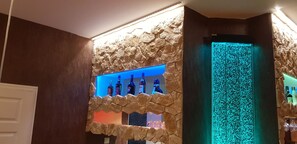 A bar area with a stone wall and a blue-lit shelf displaying bottles. - Hotel Mohr & SPA (Werder (Havel))