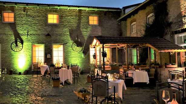 An outdoor dining area with tables and chairs, potted plants, and a stone building in the background. - Hotel Mohr & SPA (Werder (Havel))