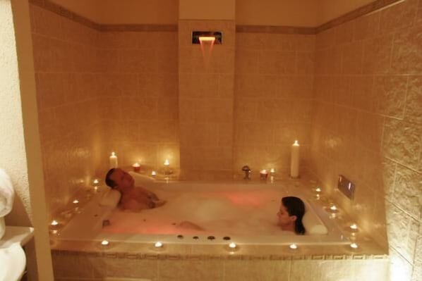 Un cuarto de spa con una bañera grande, velas y una persona relajándose.