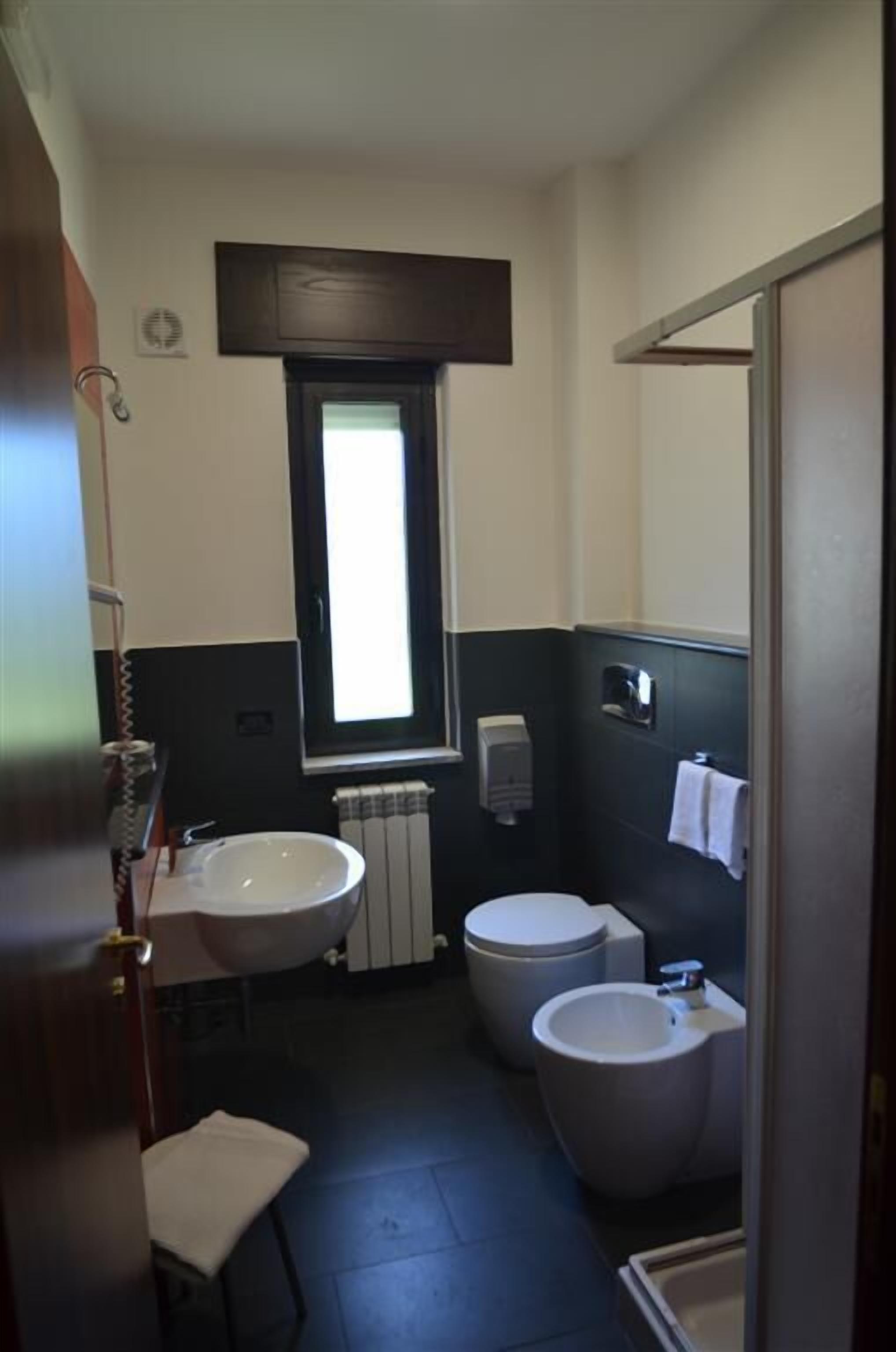 A compact bathroom with a window, two sinks, a toilet, and a towel rack.