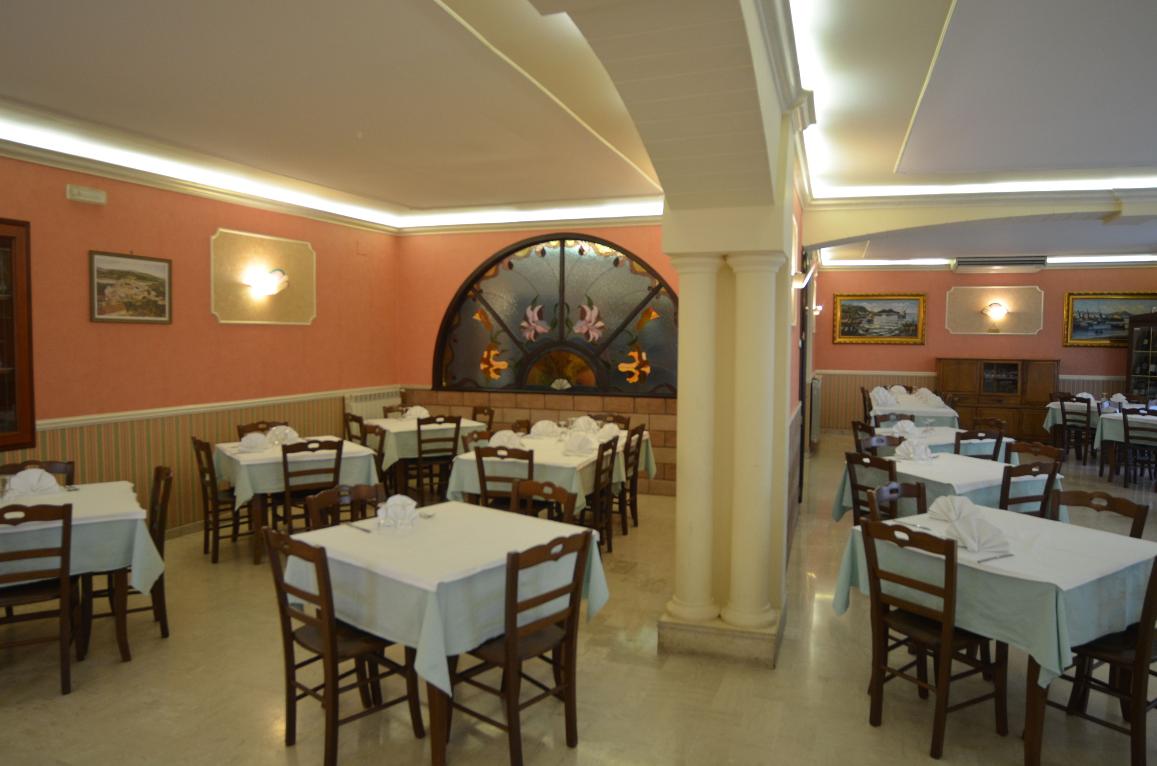 Een restaurant met meerdere tafels en stoelen, een decoratieve boog en ingelijste foto's aan de muren.