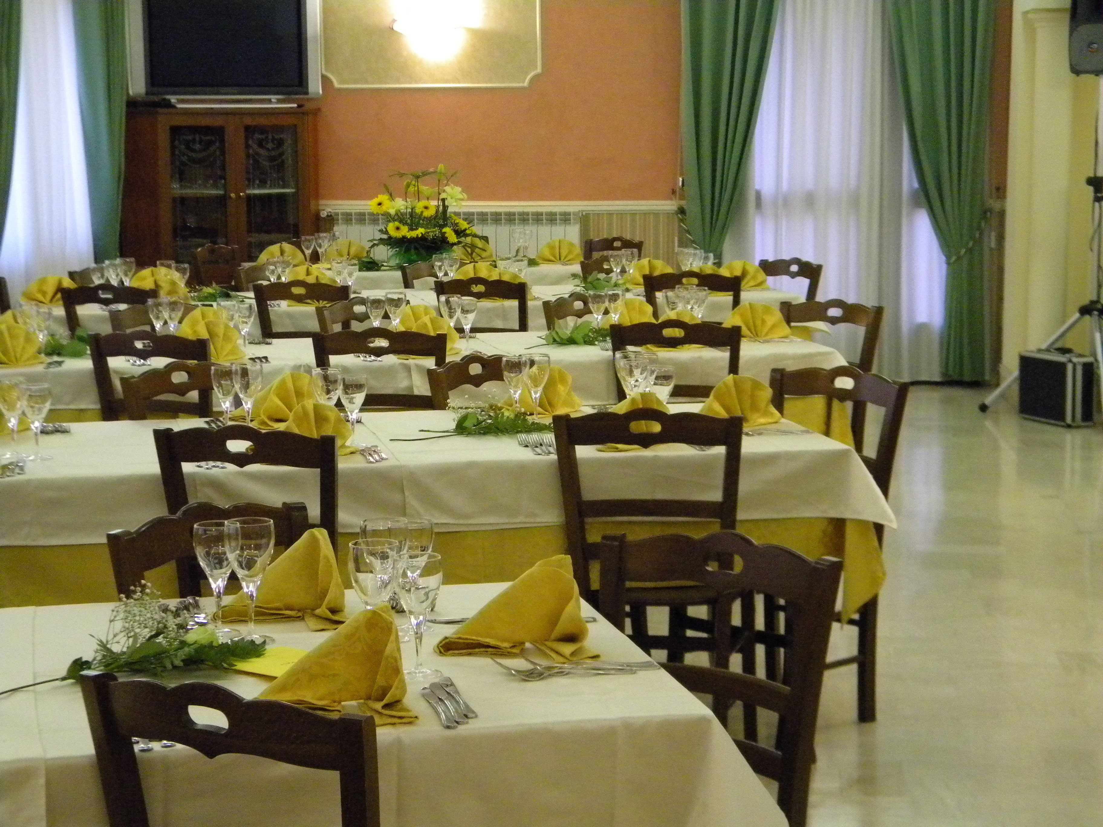 A banquet hall with multiple tables set for dining, featuring yellow napkins and clear glassware.