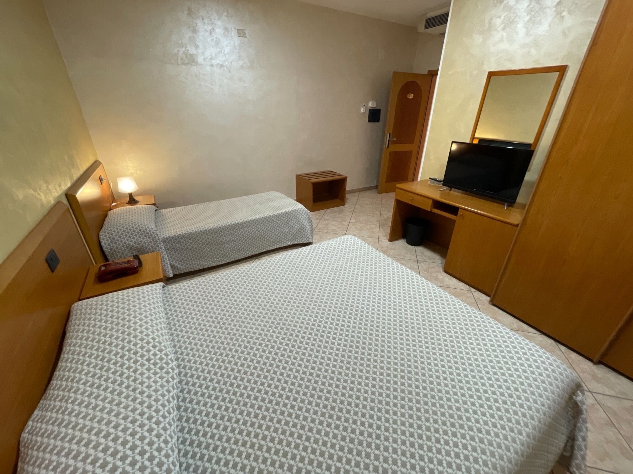 Camera d'albergo con due letti, una scrivania, una sedia, una televisione e un cestino.
