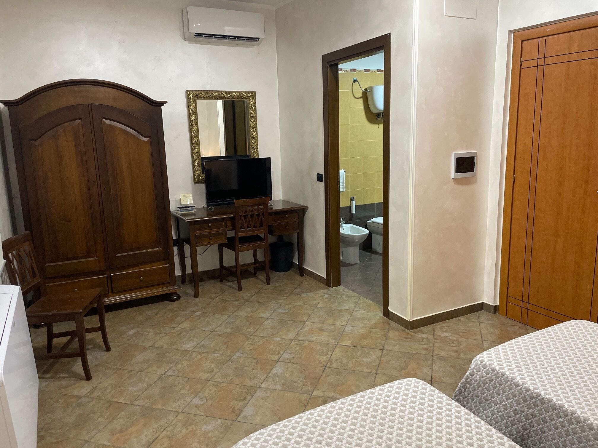 Una habitación con un armario de madera, un escritorio con una silla, un televisor y una cama con colcha estampada.
