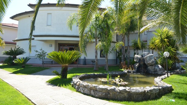 Un jardín ajardinado con un estanque, palmeras y un edificio con fachada curva.