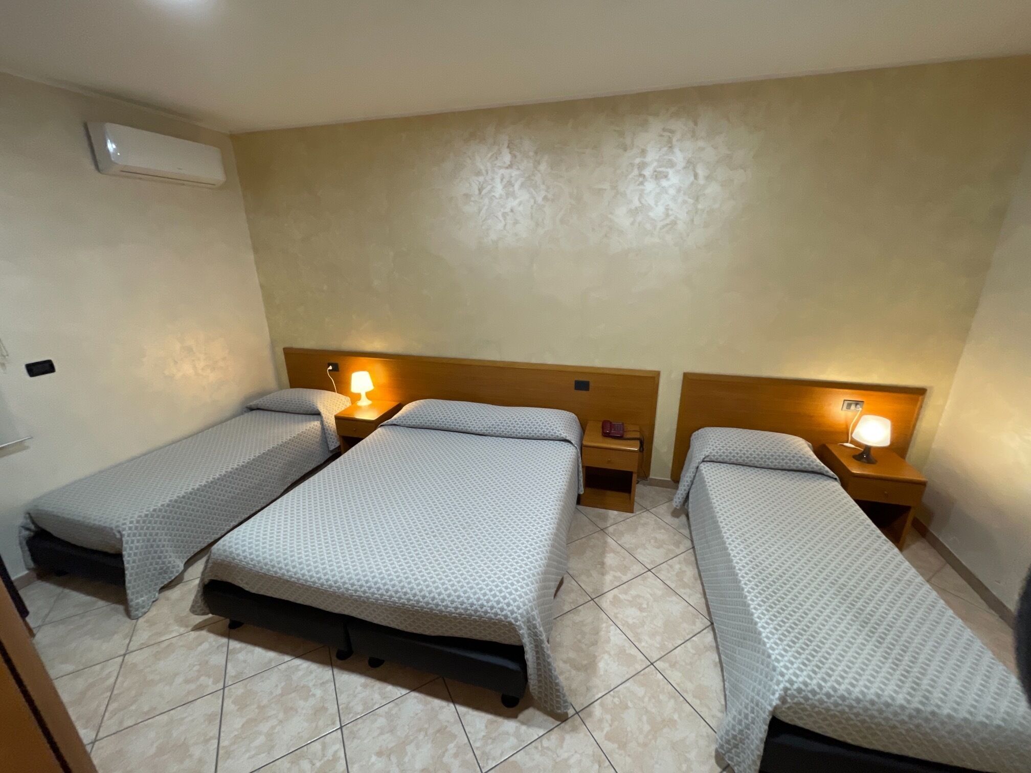 A hotel room with three single beds, each with a nightstand and a table lamp.
