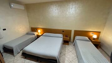 A hotel room with three single beds, each with a nightstand and a table lamp.