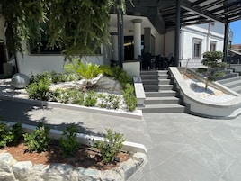 Un edificio moderno con un área exterior cubierta, escalones de piedra y diversas plantas.