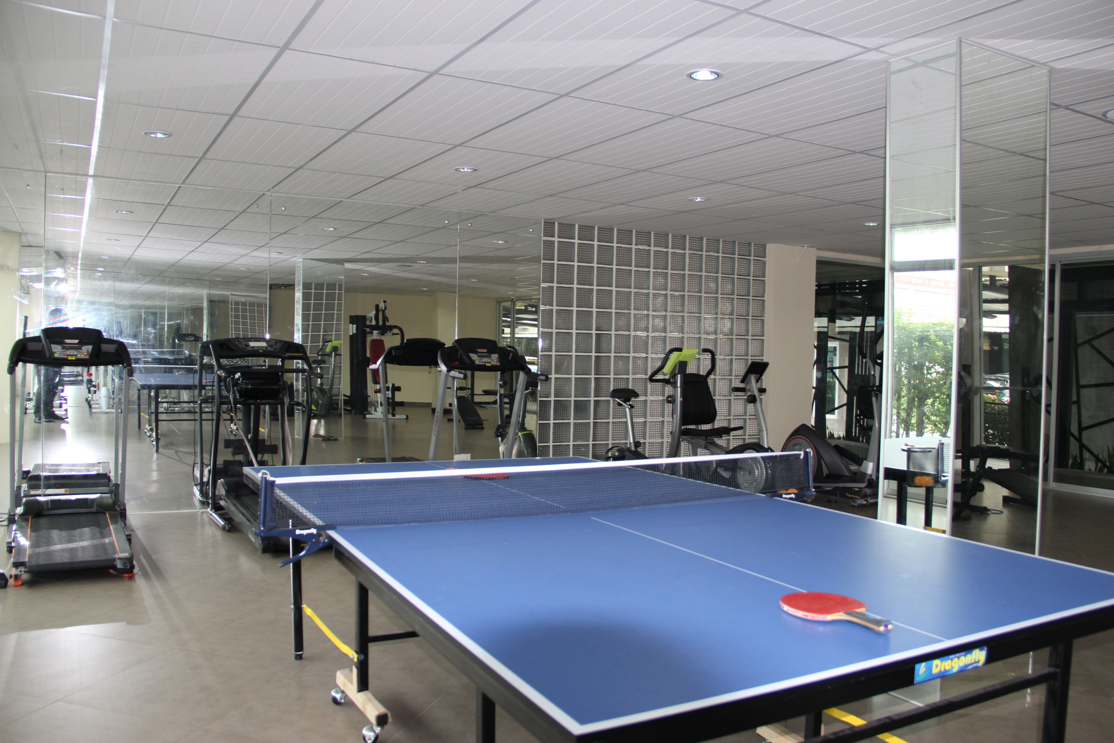Un gimnasio con mesa de ping pong, cintas de correr y equipo de ejercicio.