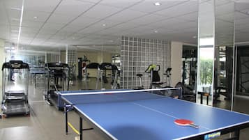 Un gimnasio con mesa de ping pong, cintas de correr y equipo de ejercicio.