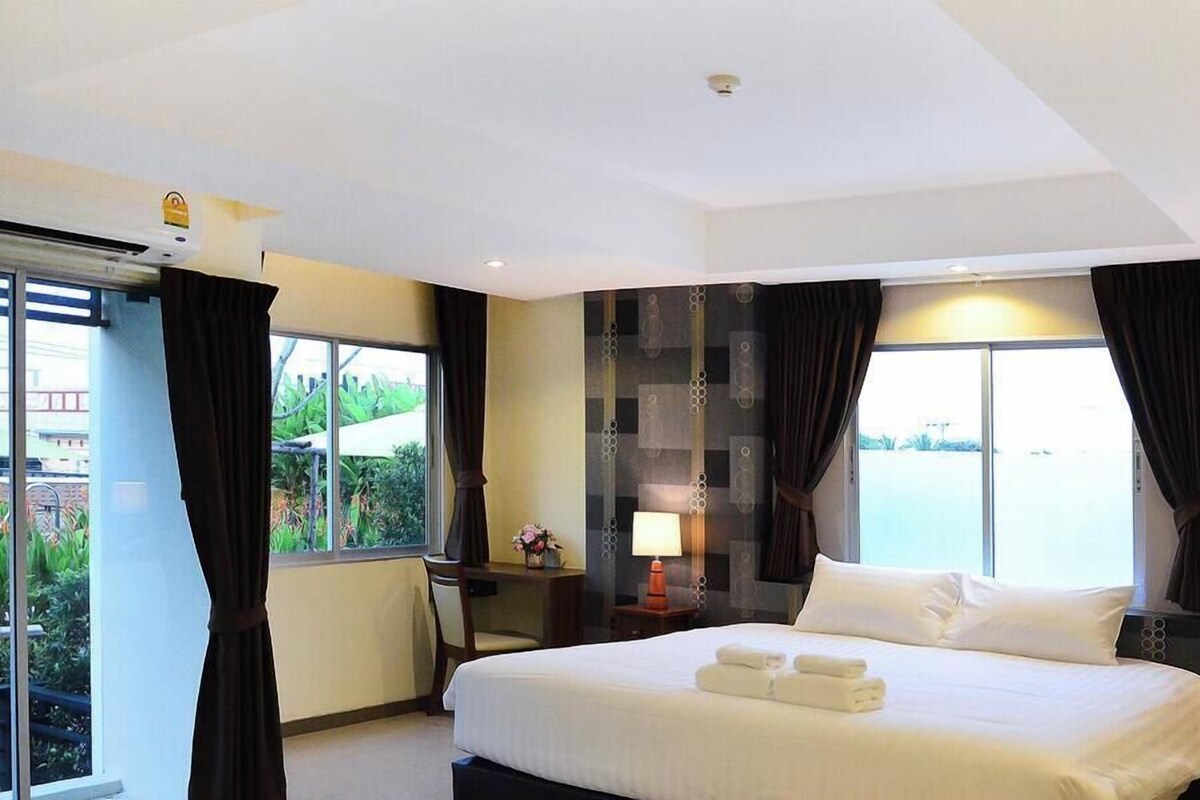 A hotel room with a bed, a desk, a chair, a lamp, and a view of the outdoors.