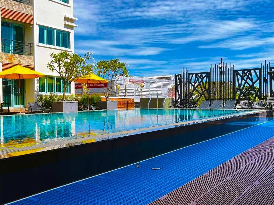 Una piscina con sillones y sombrillas, rodeada por un edificio moderno con balcones y un cielo despejado.