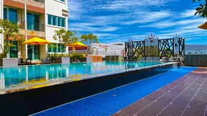 A swimming pool with lounge chairs and umbrellas, surrounded by a modern building with balconies and a clear sky. - Suvarnabhumi Ville Airport Hotel (Bang Phli)