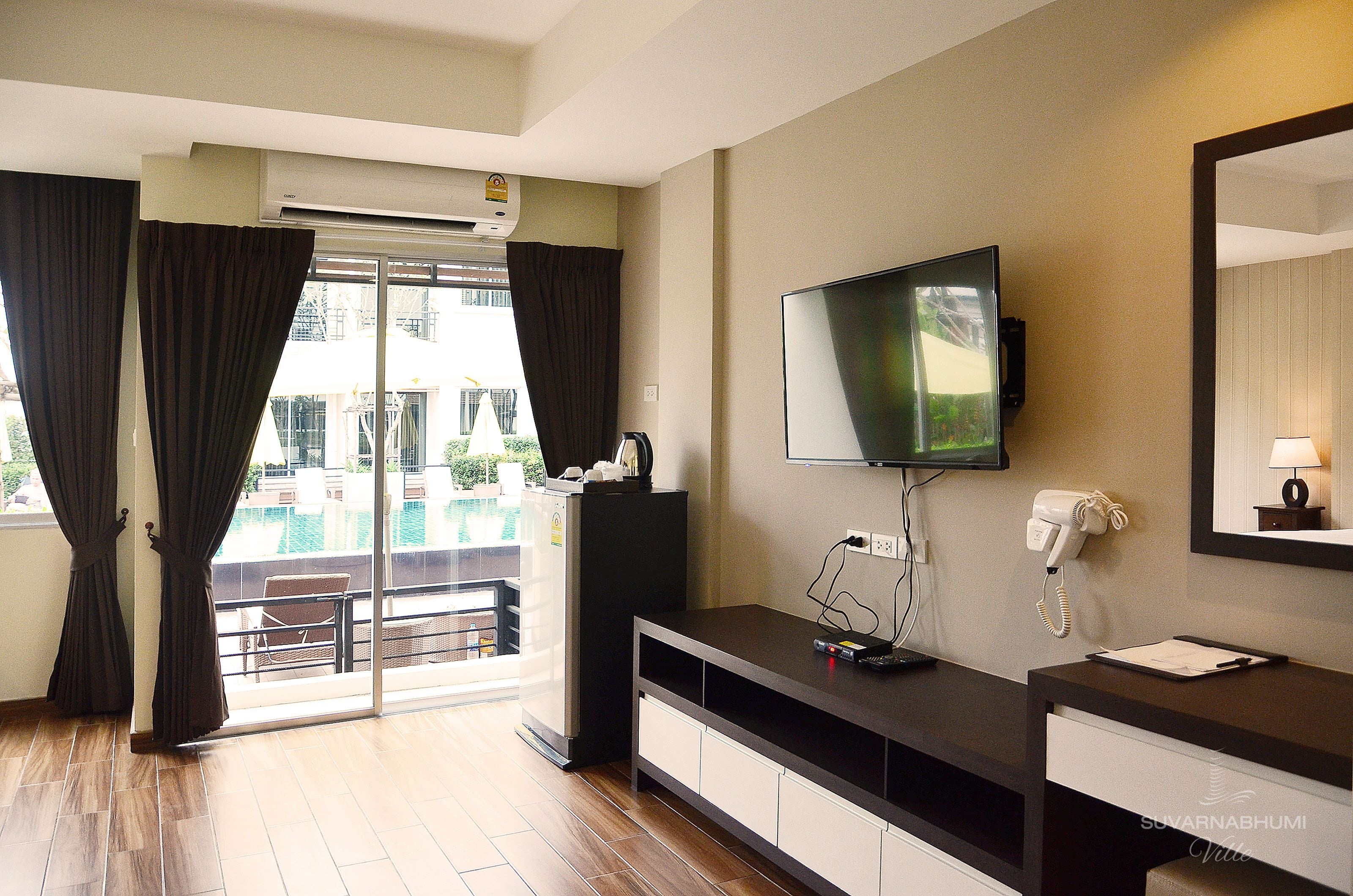 A hotel room with a large TV, a desk with a phone, and a view of a swimming pool through the glass door.