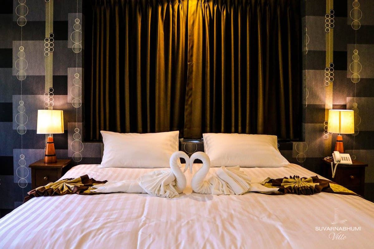 A hotel room with a bed, two pillows, a nightstand with a lamp, and a wall with a geometric pattern.