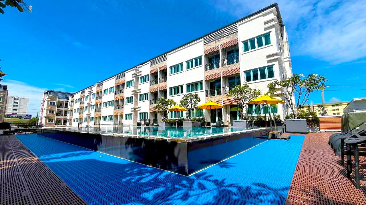 A modern hotel with a swimming pool, outdoor seating, and a clear blue sky.
