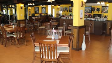 Un restaurante con mesas y sillas de madera, una zona de bar y paredes amarillas.