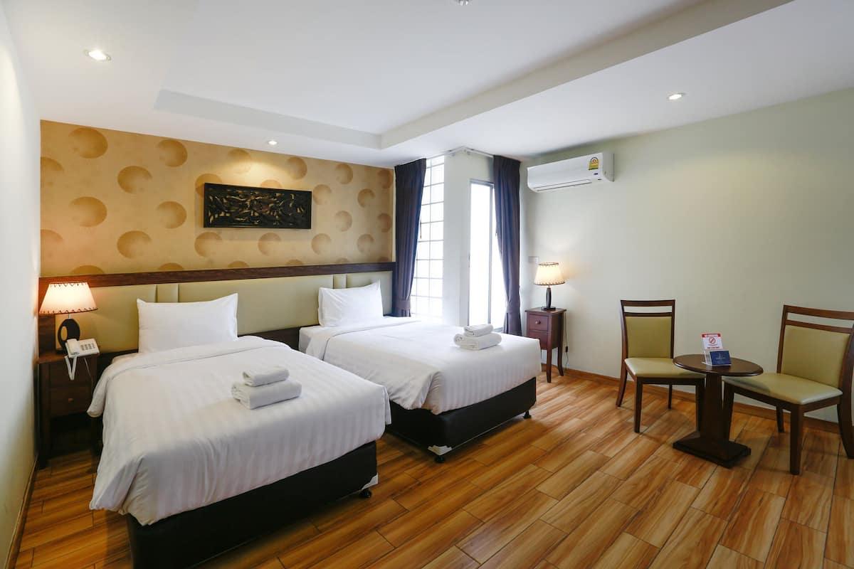 A hotel room with two beds, a small table, chairs, a phone on the nightstand, and an air conditioning unit on the wall.