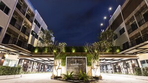 Ein moderner Hotelzugang mit einer zentralen Beschilderung, umgeben von Grünpflanzen und beleuchtet durch Straßenlaternen.