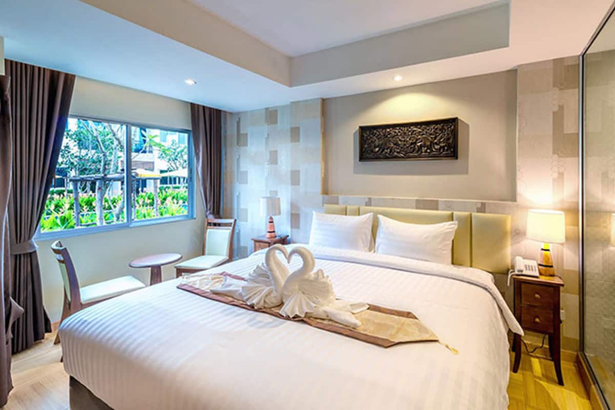A hotel room with a large bed, a small table, a chair, and a window with curtains.