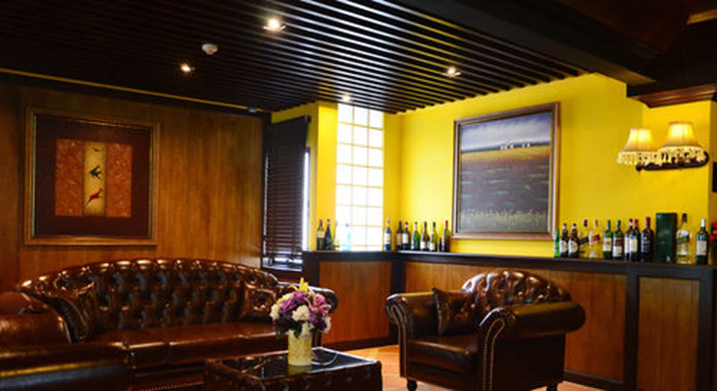 A bar area with leather sofas, a bar counter with bottles, and a large painting on the wall.
