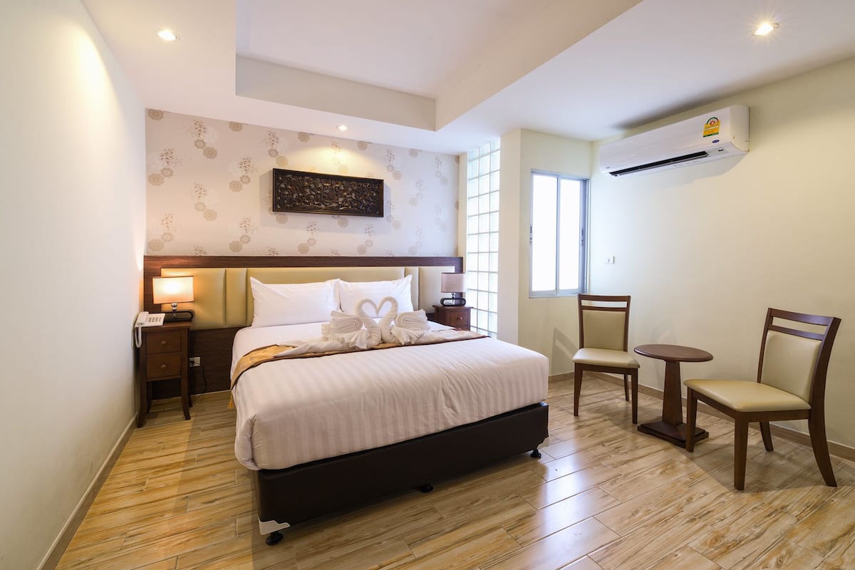 A hotel room with a bed, bedside tables, a chair, and an air conditioning unit.