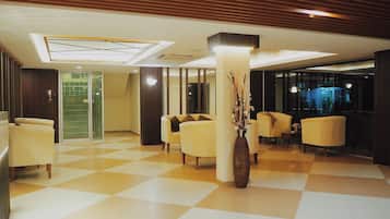 Un vestíbulo de hotel con suelo a cuadros, varios sofás, un jarrón grande y una partición de vidrio.
