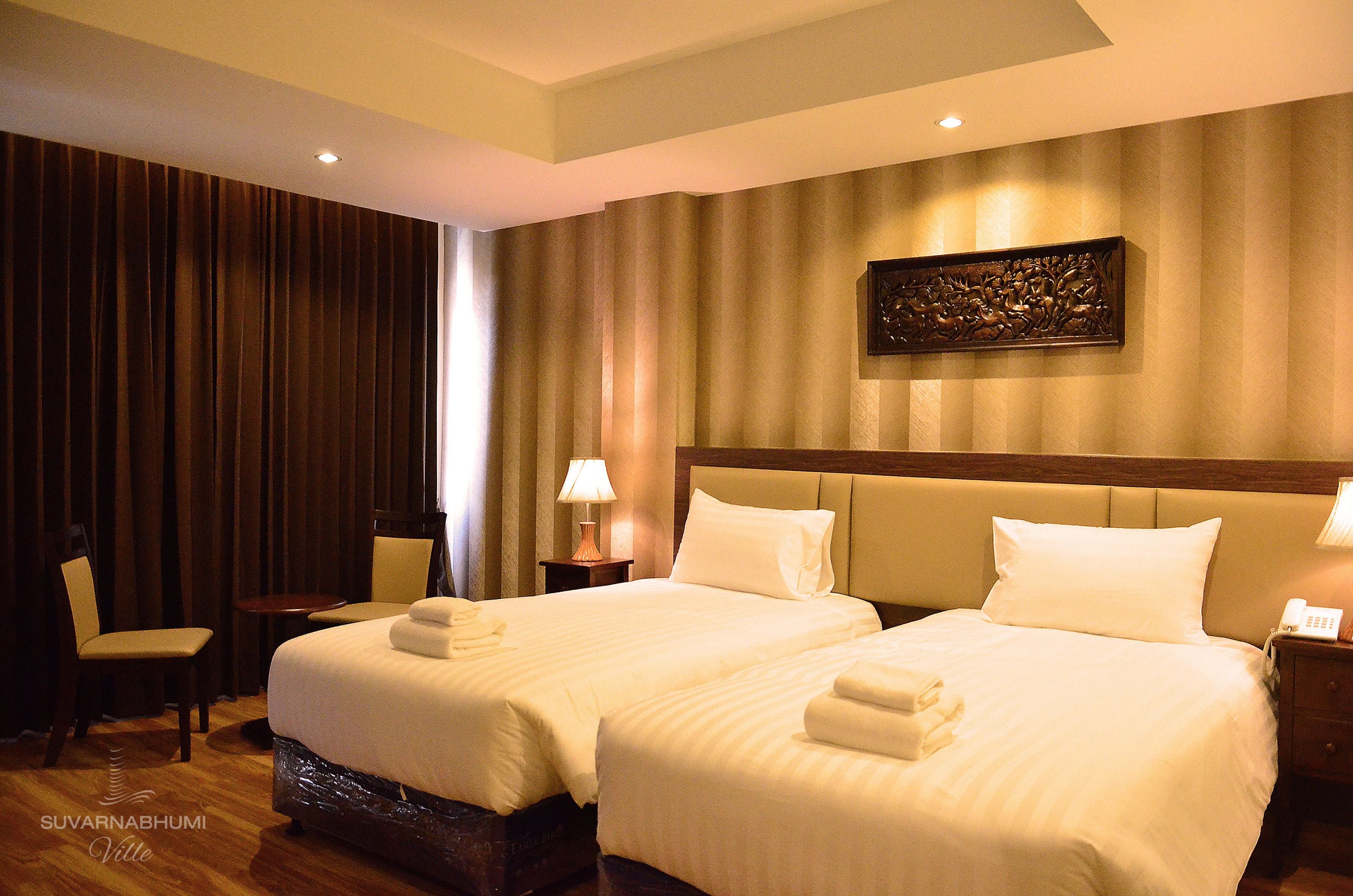 Habitación de hotel con dos camas, una silla, una mesita y una obra de arte colgada en la pared.