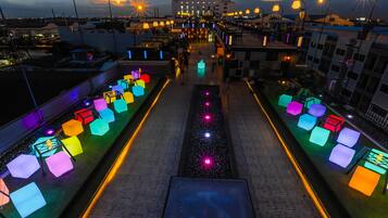 Una terraza en la azotea con zonas de estar iluminadas de colores y un paseo central.