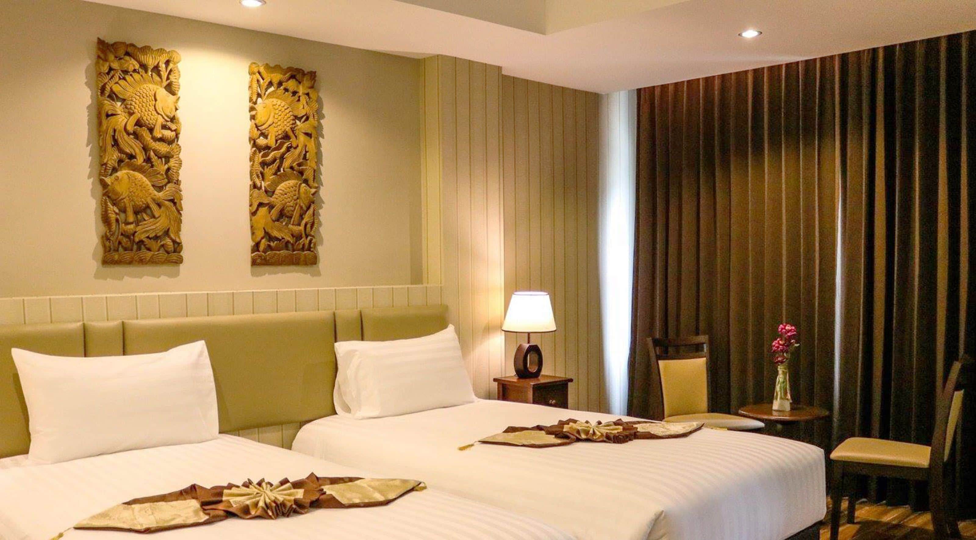 A hotel room with two beds, a nightstand with a lamp, a chair, a vase with flowers, and decorative wall panels.