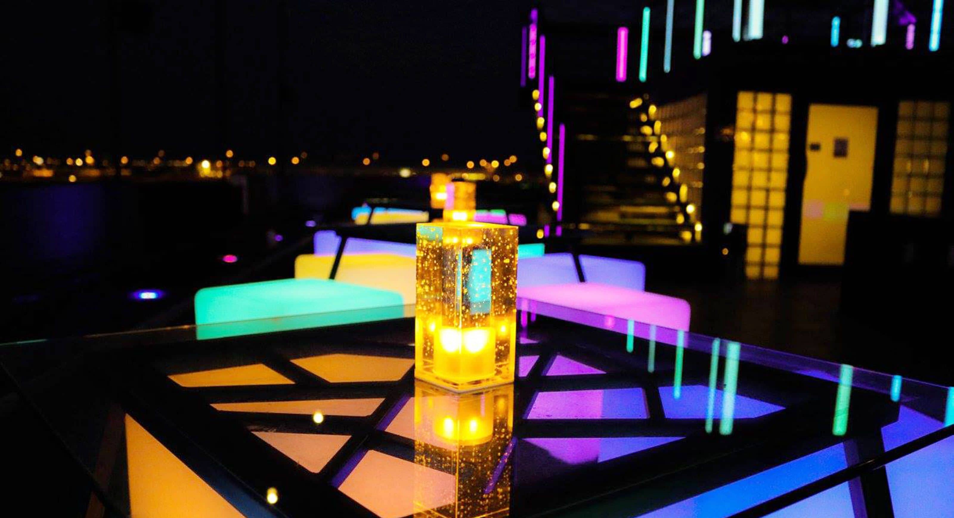 A modern lounge area with a central table, colorful seating, and a staircase in the background.