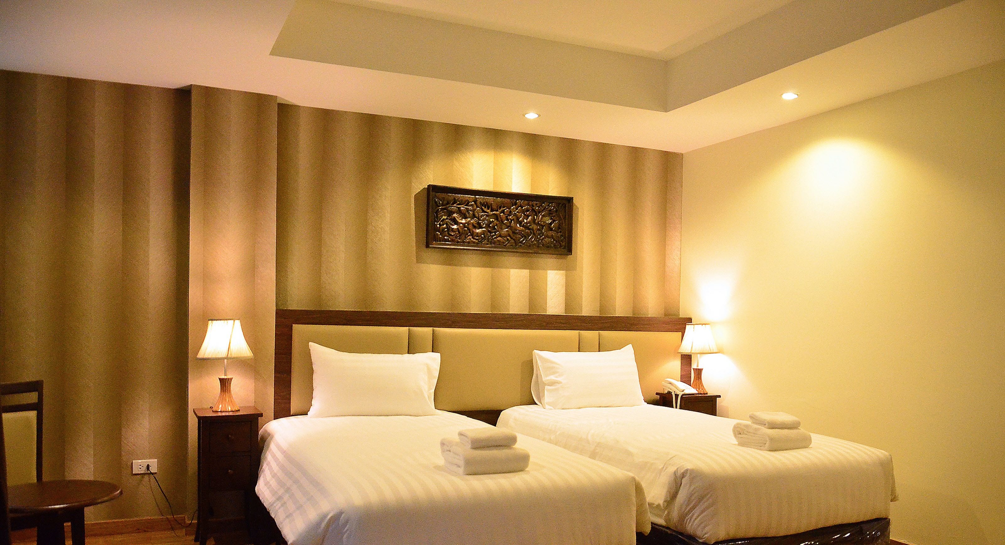 Une chambre d’hôtel avec deux lits, une tête de lit, des lampes de chevet, une œuvre d’art accrochée au mur et une chaise.
