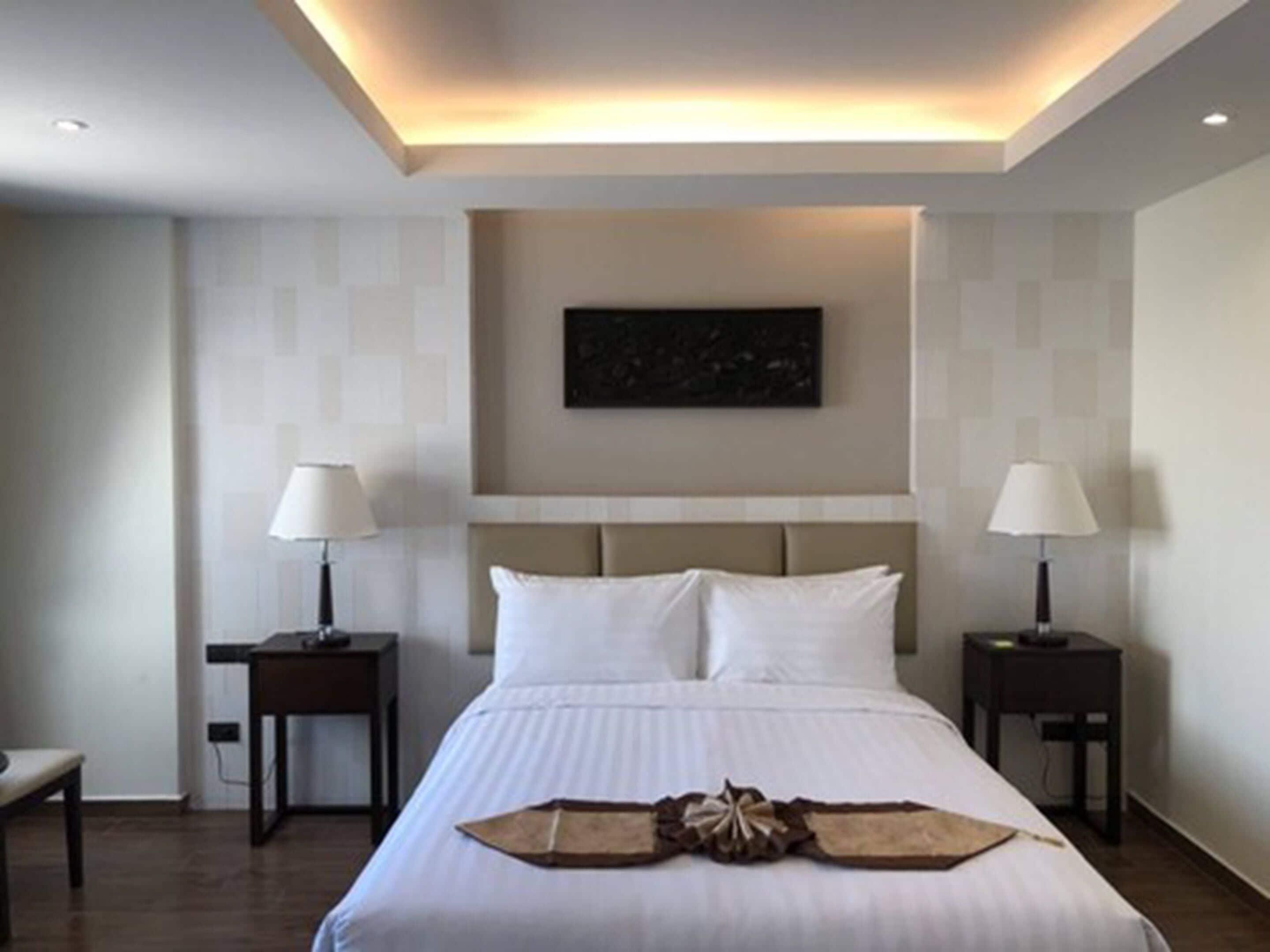 A hotel room with a large bed, two bedside tables with lamps, a headboard, and a wall-mounted artwork.