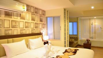 A hotel room with a bed, a nightstand, a lamp, a bathroom with a shower, and a wall with framed pictures.