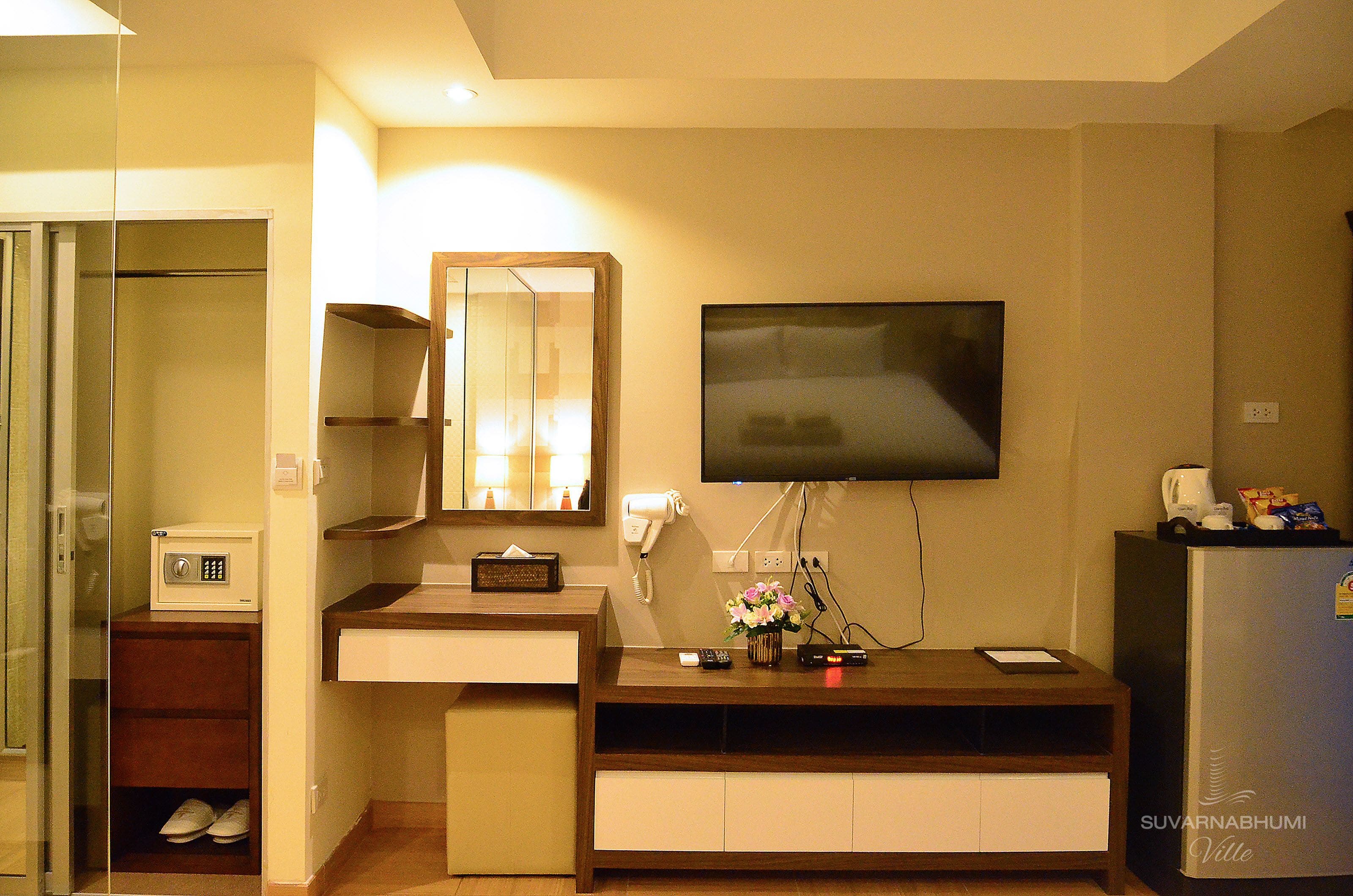 Quarto de hotel com televisão na parede, micro-ondas, uma pequena mesa com um vaso de flores e um sapateiro.