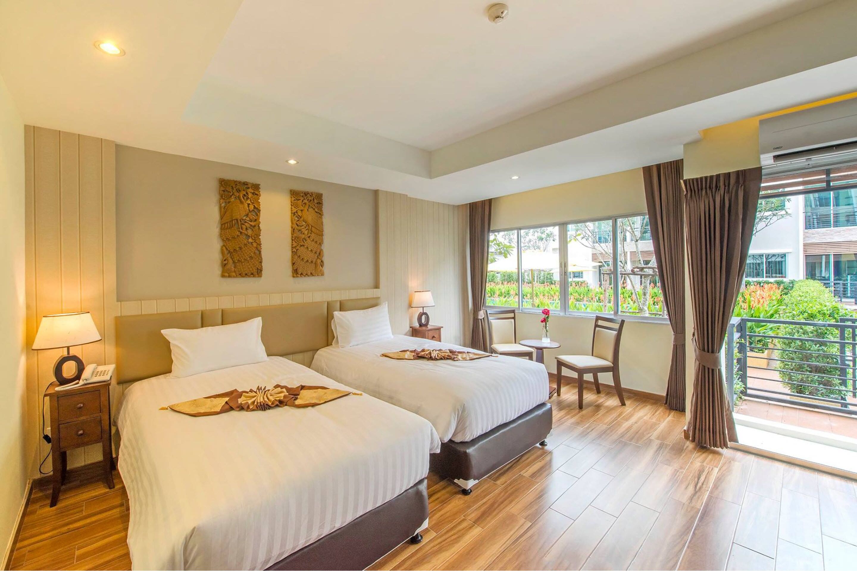 Quarto de hotel com duas camas, uma mesinha, uma cadeira e varanda com vista para o verde.